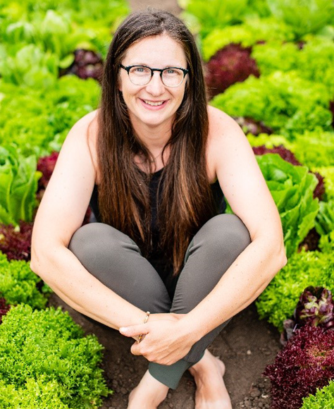 Owner Jenny Quiner sitting in a row of her crops at DUG