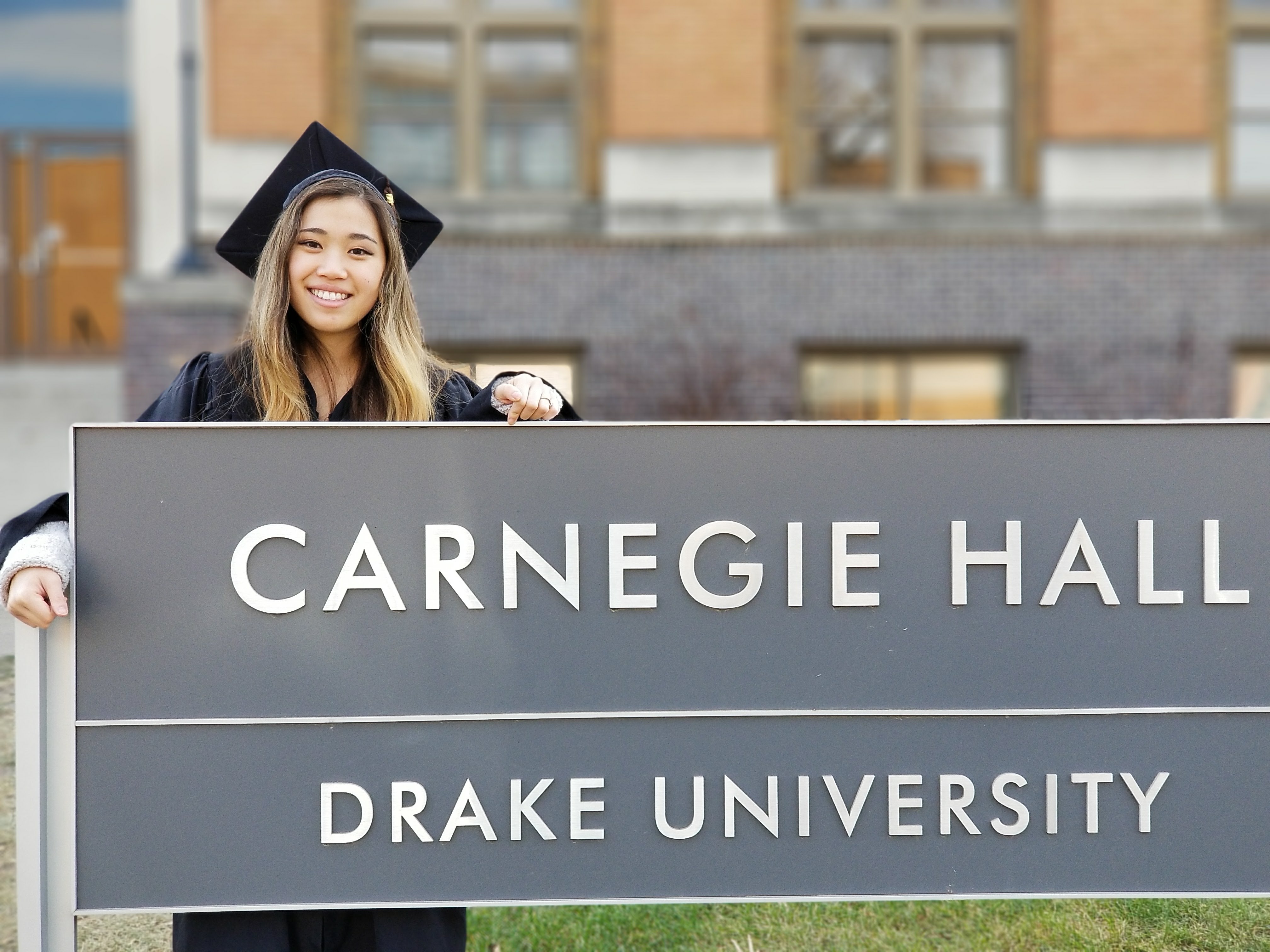 Linzi standing behind a Drake University sign in her cap and gown