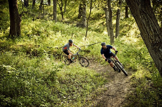 Two cyclists going down a nature trail on their bikes