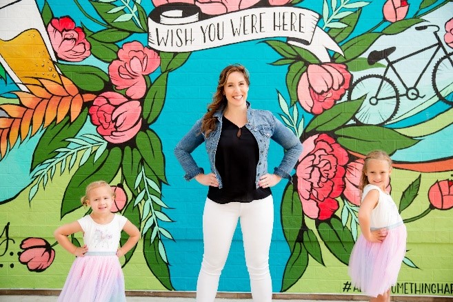 Lydia standing in front of a wall mural smiling with her two daughters