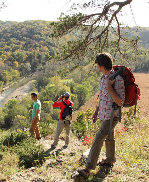 Three young men hiking in Iowa look down over a flowing river