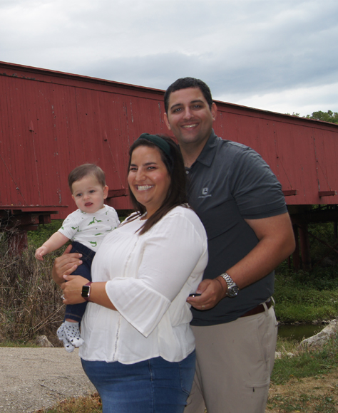 Family standing in front of covered bridge smiling