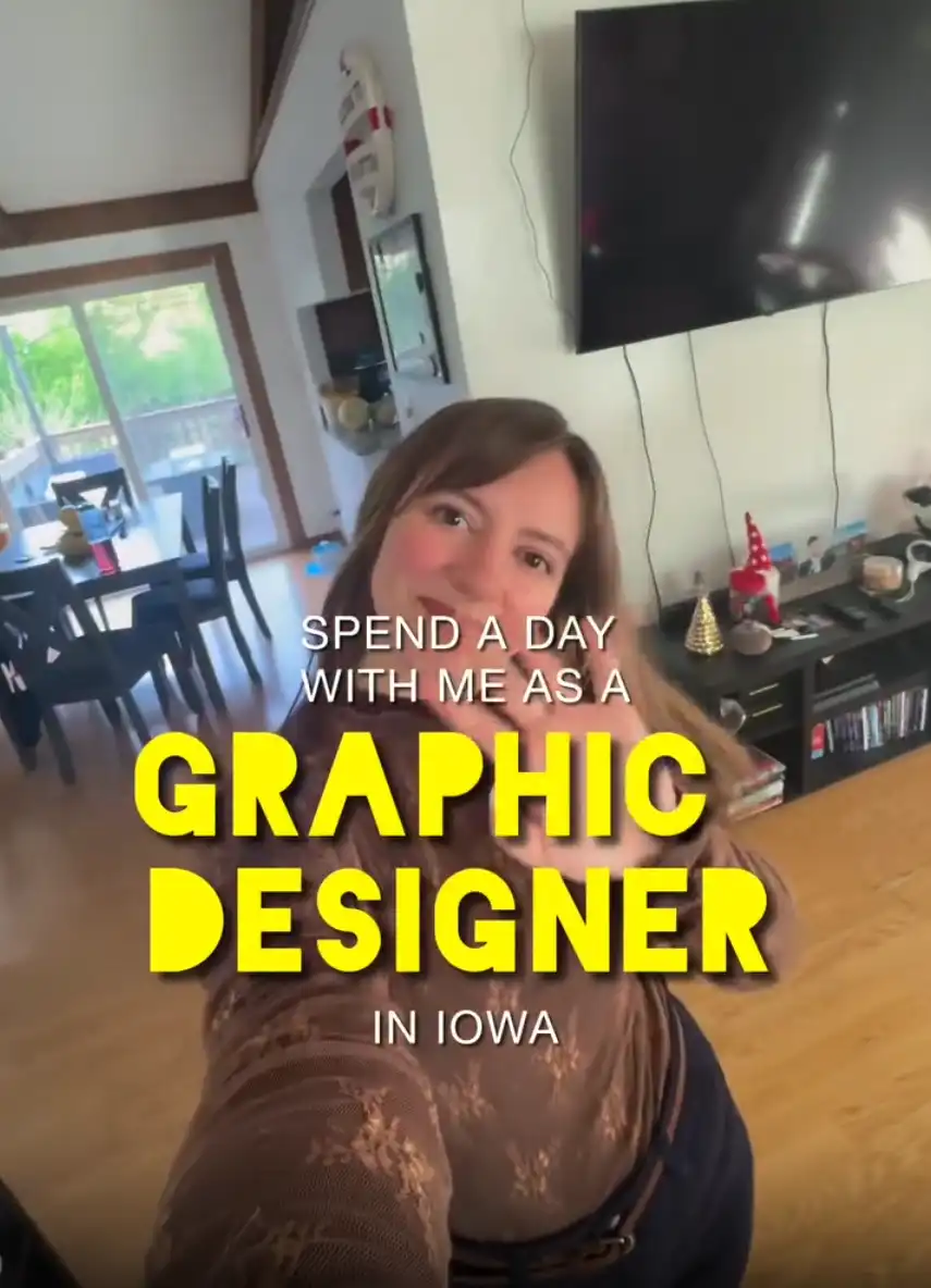 A woman waving to the camera with text overlay saying "spend a day with me as a graphic designer in Iowa"