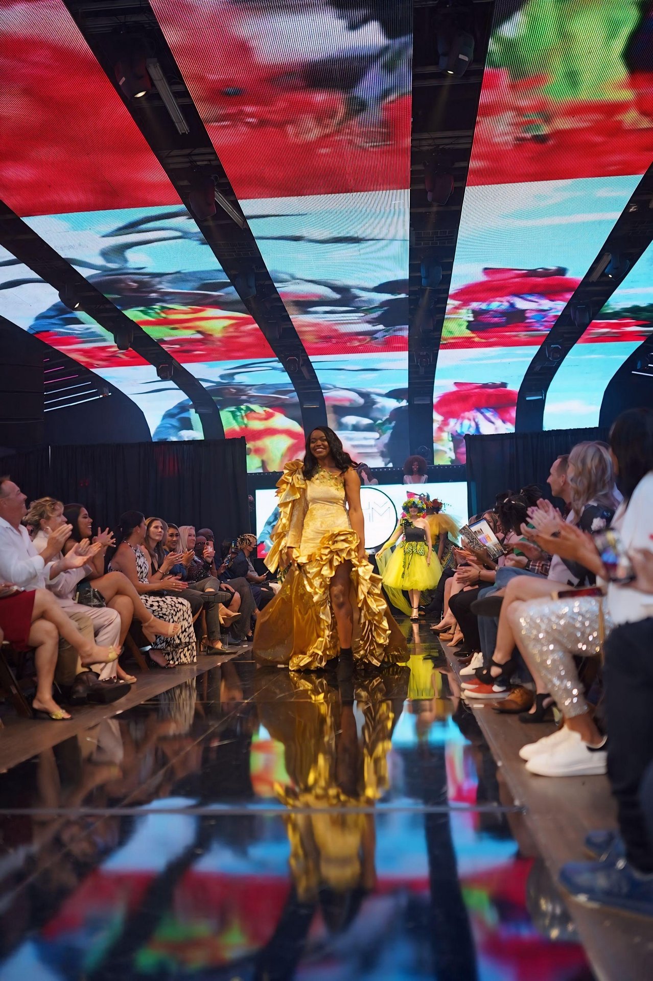 Model walking on a runway wearing a yellow dress