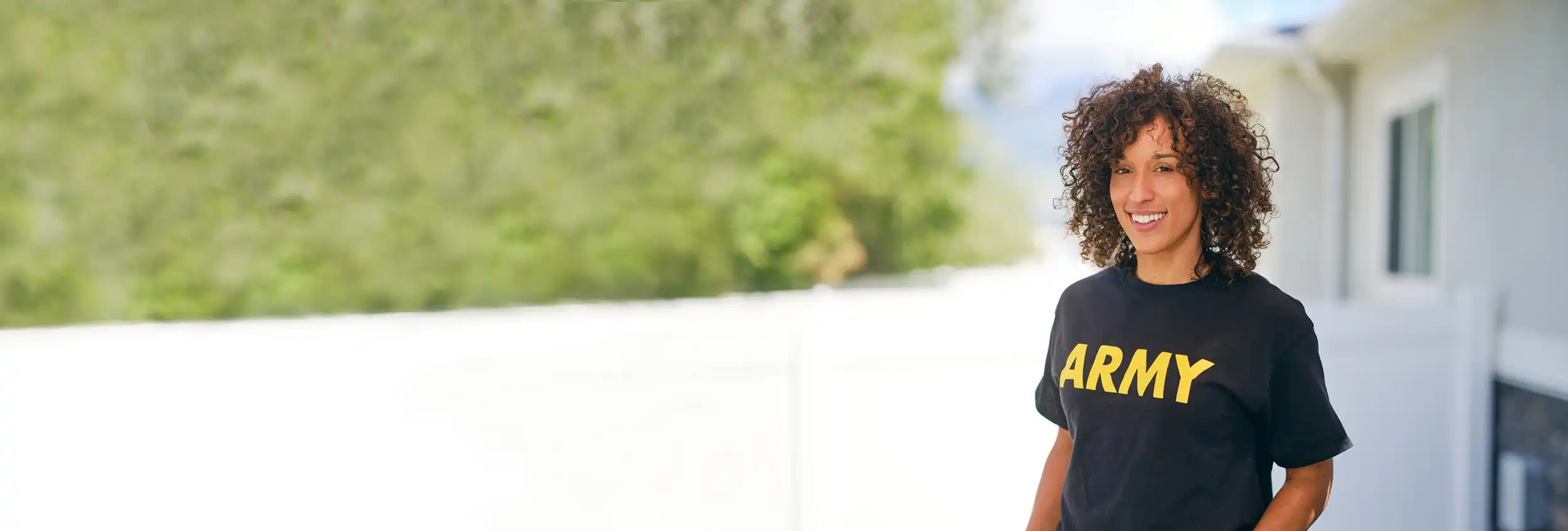 A smiling woman in an Army t-shirt stands outdoors