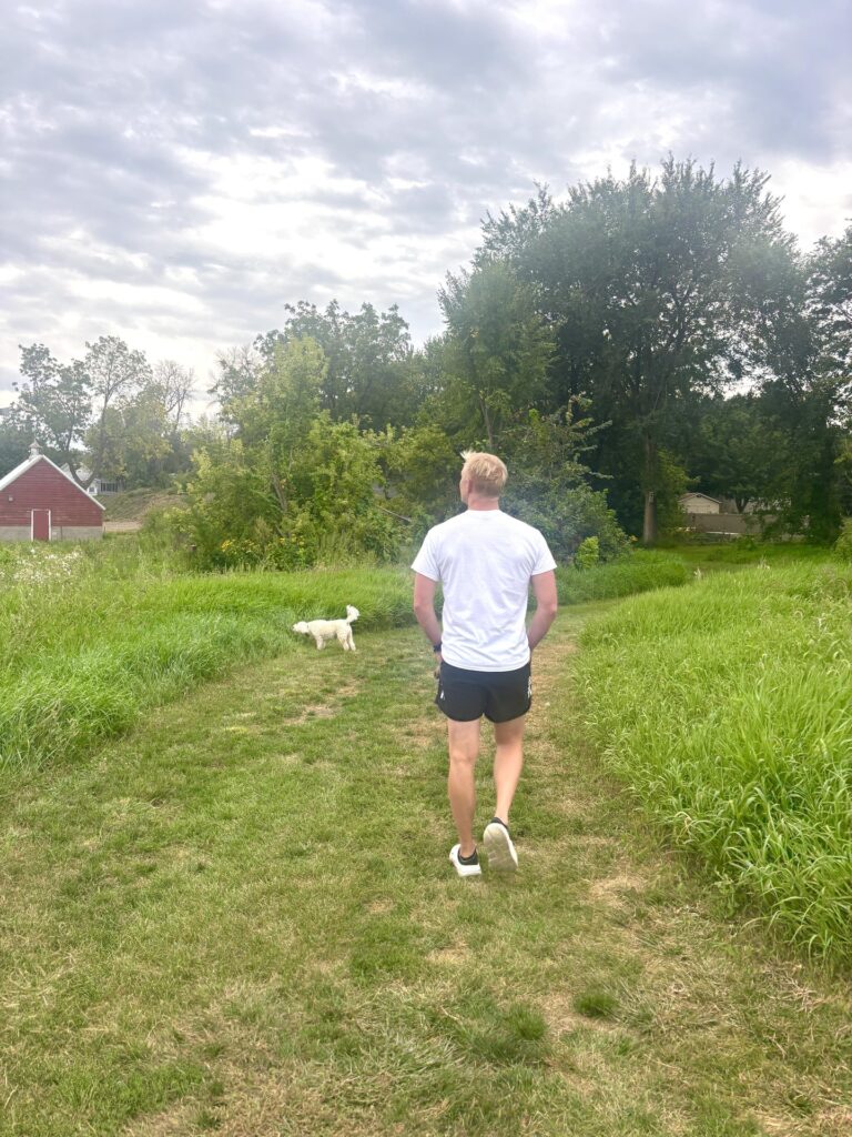 A man and a dog walking on a grassy trail