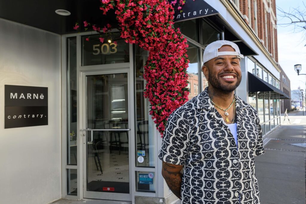 Billy Weathers smiles outside the Contrary storefront, wearing a geometric patterned shirt and a white cap.