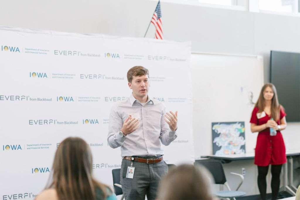 Cody Butenhoff spreaks to a group of individuals in front of an Iowa Economic Development Authority background