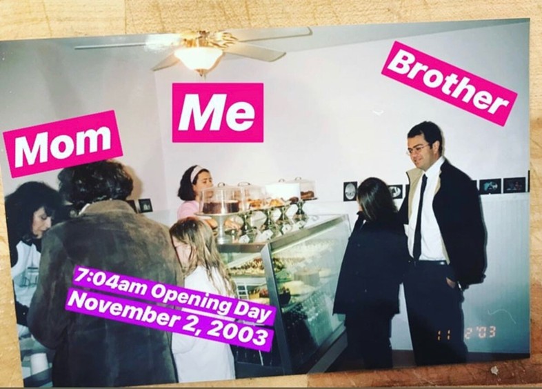 Image from 2003 showing a bakery opening day with pink labels identifying mom, me, and brother among the staff and customers.