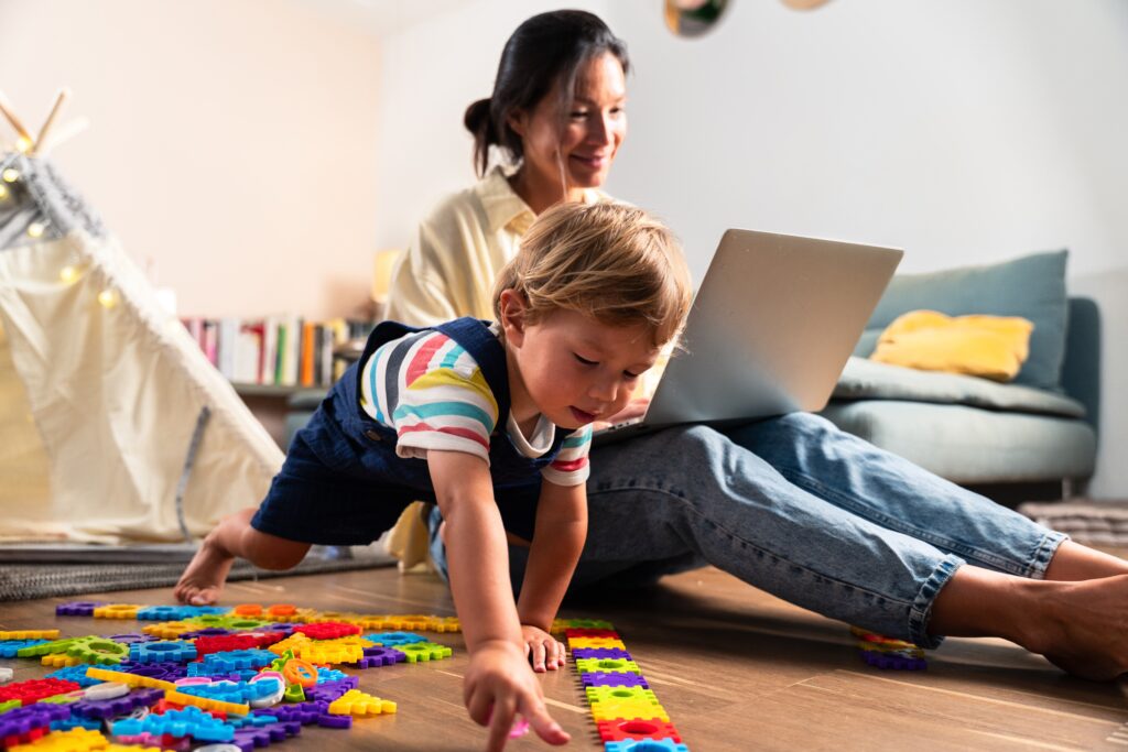 mom working on a laptop while child plays with toys